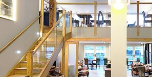 A multi-level interior with a wooden staircase, seating areas, and large windows offering views.
