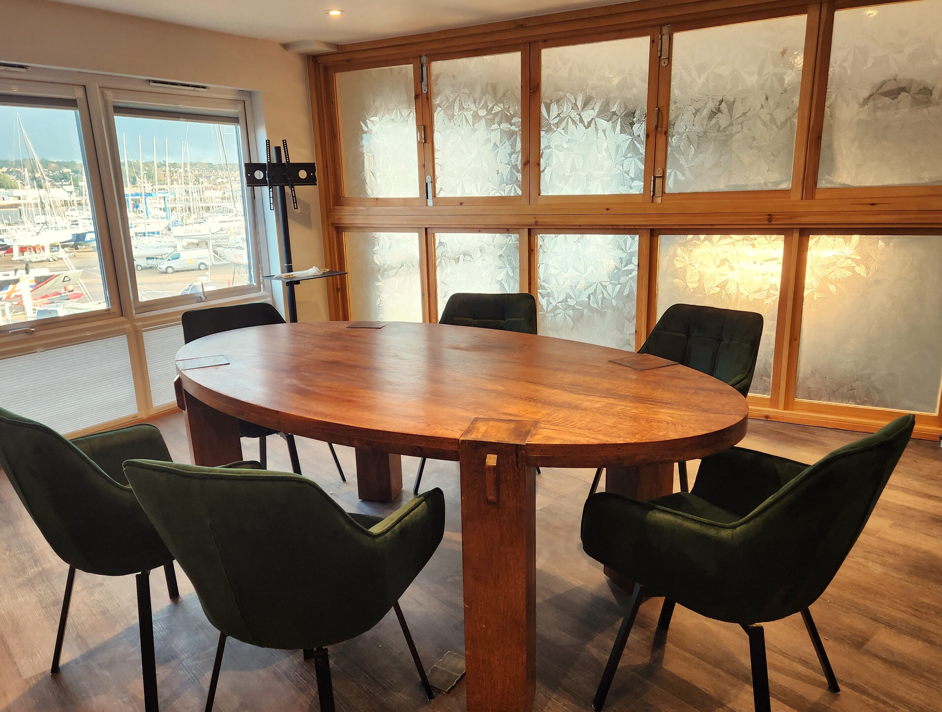 A conference room with a large wooden table and six green chairs.