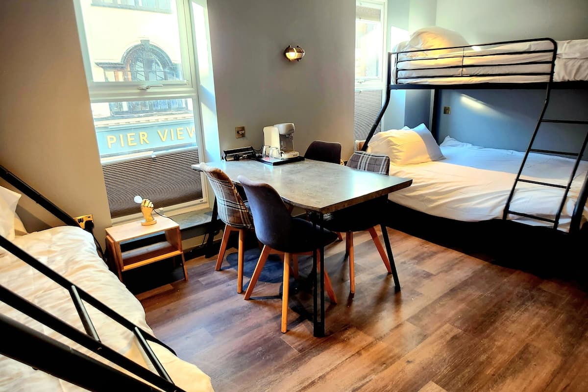 Habitación compacta con literas, una pequeña mesa con sillas, una máquina de café y una ventana con vistas a un edificio que dice "PIER VIEW".