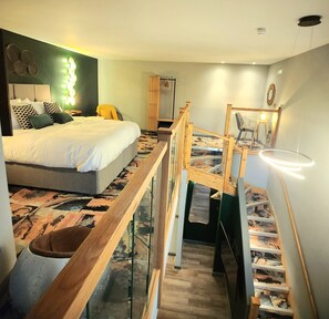 Un dormitorio con una cama, un banco de madera, una escalera y un aplique de pared.