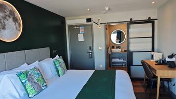A hotel room with a bed, a desk, a chair, a mirror, and a bathroom with a sink and toilet.