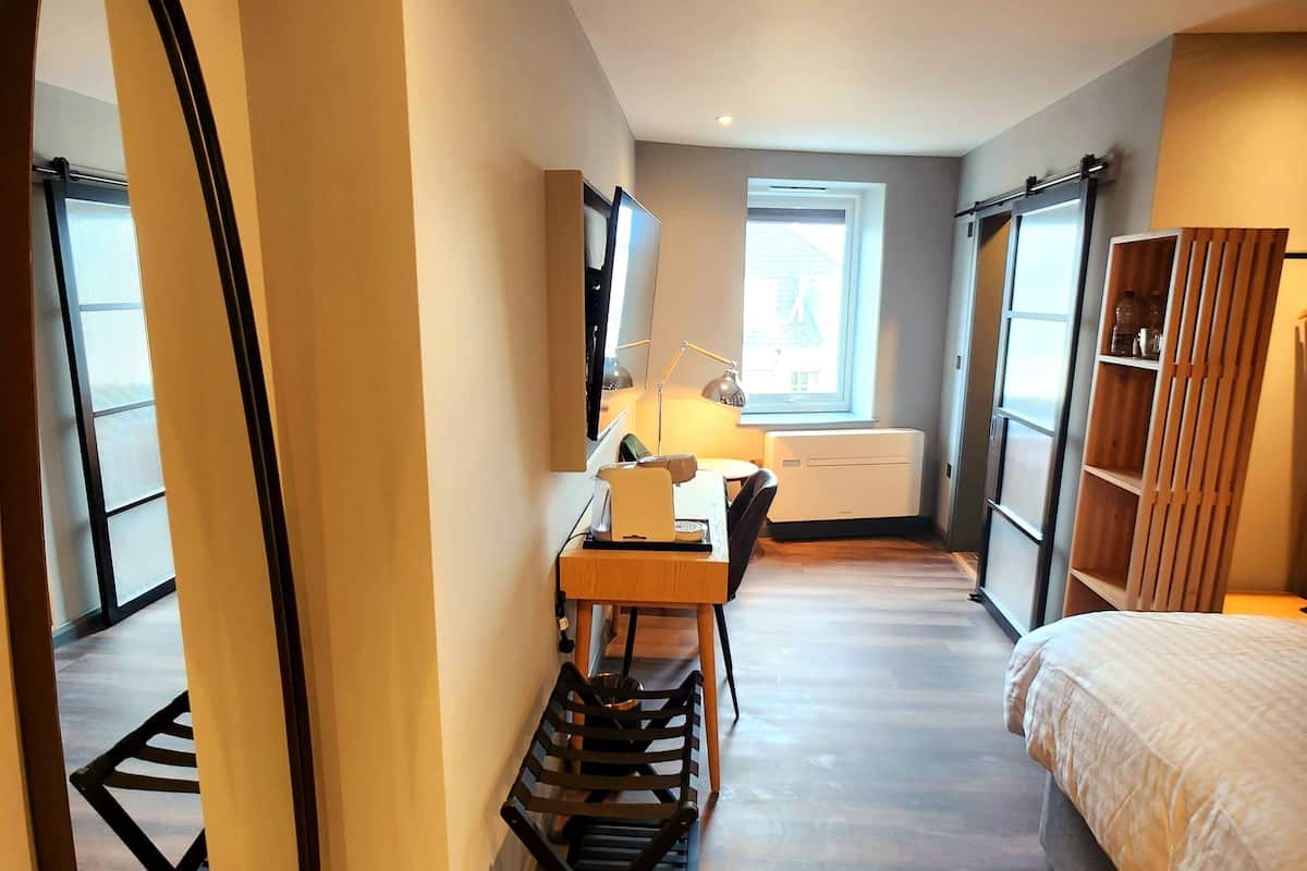 Un dormitorio con cama, escritorio, silla, espejo y ventana.
