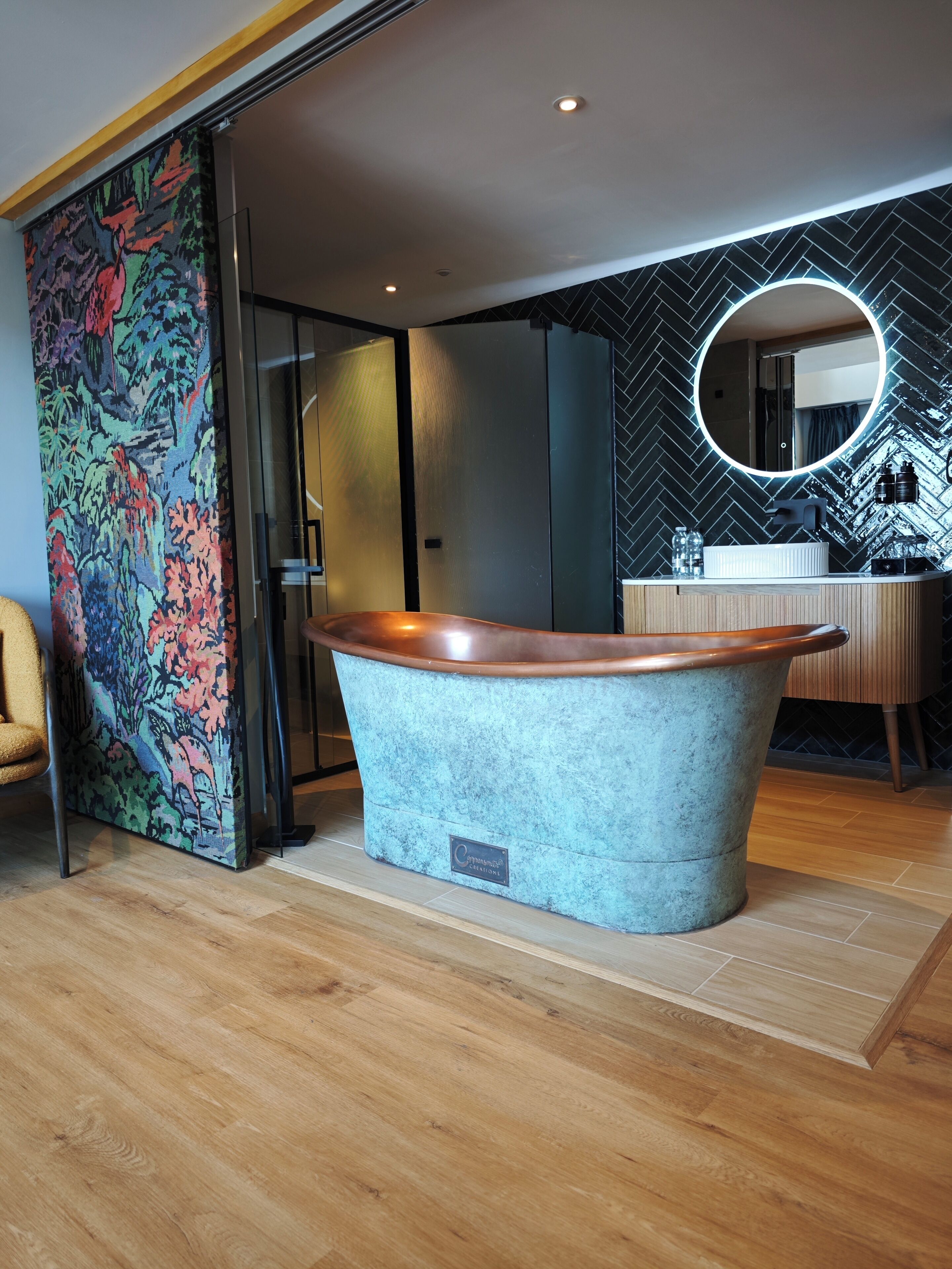 A modern bathroom with a freestanding bathtub, a round mirror, and a herringbone-patterned wall.