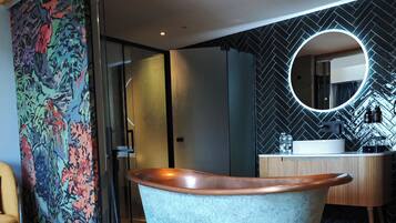 A modern bathroom with a freestanding bathtub, a round mirror, and a herringbone-patterned wall.