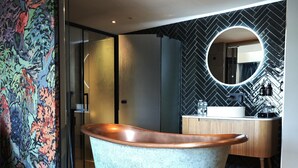 A modern bathroom with a freestanding copper bathtub, a round mirror, and a herringbone-patterned wall.