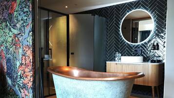 A modern bathroom with a freestanding copper bathtub, a round mirror, and a herringbone-patterned wall.