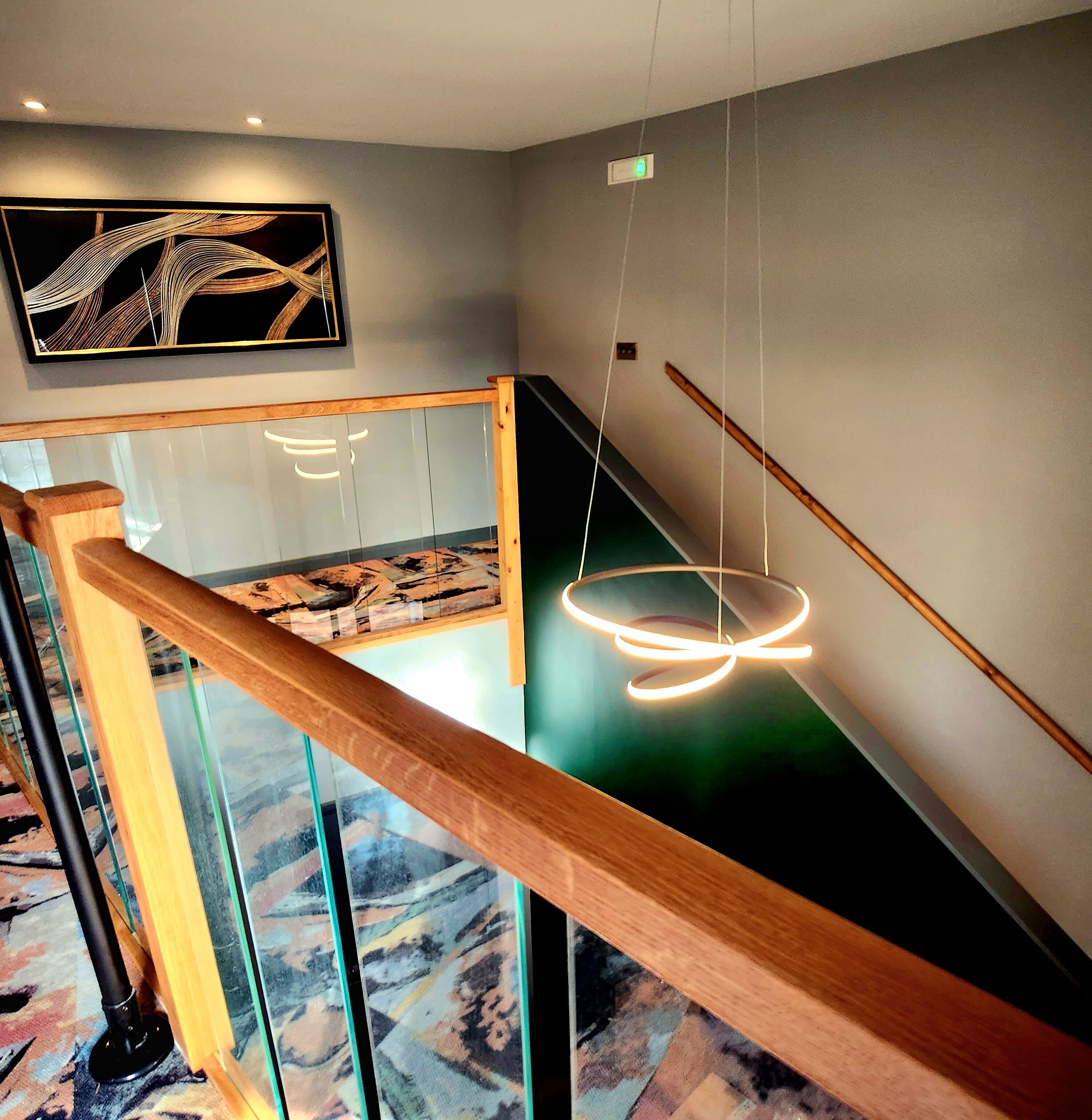 Een modern interieur met glazen balustrade, een hanglamp en een aan de muur bevestigd schilderij.