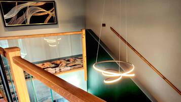Een modern interieur met glazen balustrade, een hanglamp en een aan de muur bevestigd schilderij.