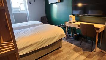 Habitación de hotel con cama, escritorio, silla, televisión y ventana.