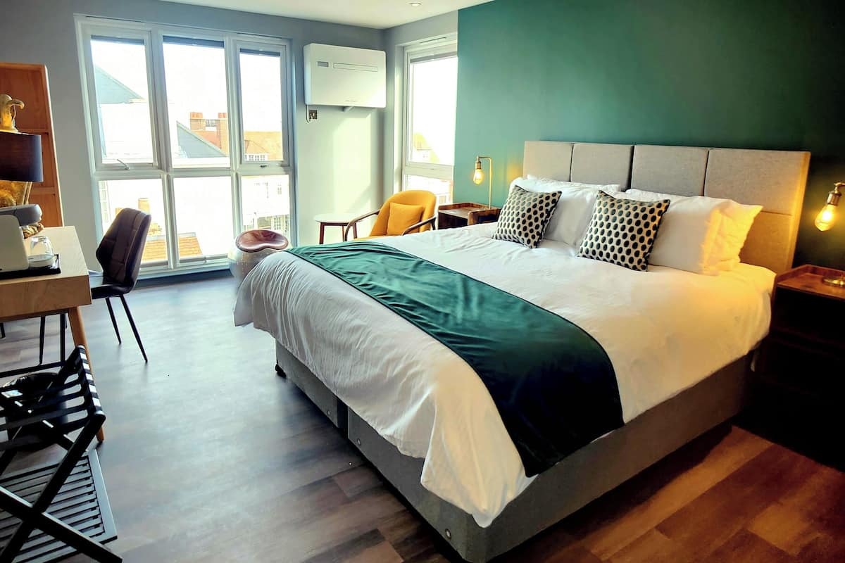 Habitación de hotel moderna con una cama grande, un escritorio y una silla. Se ven edificios a través de las ventanas.