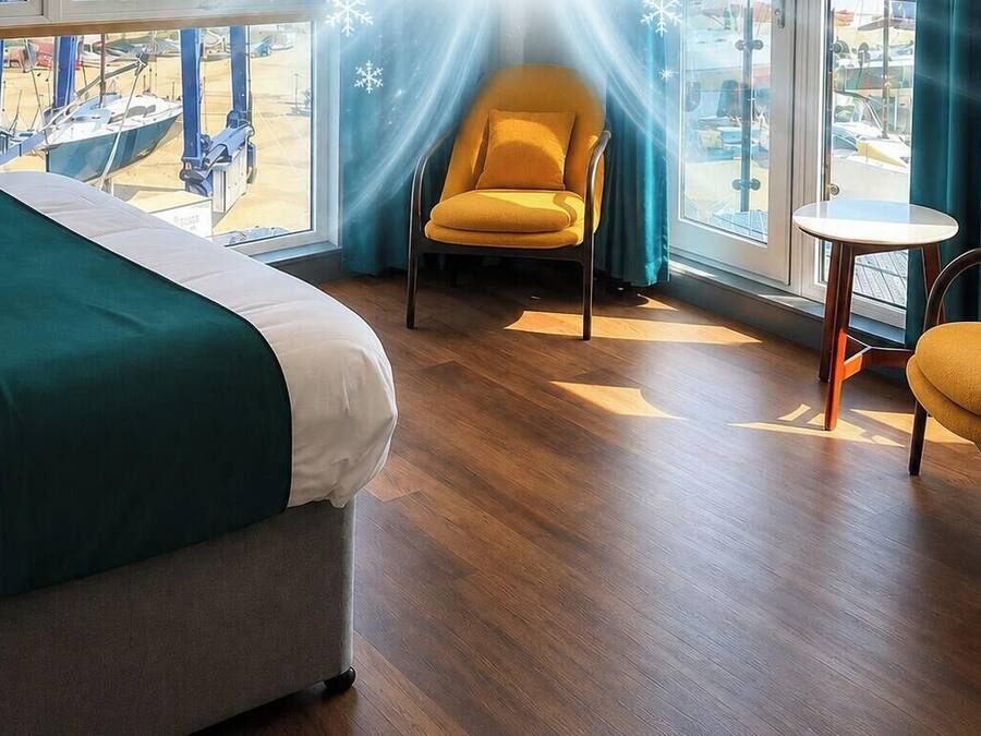 Hotelkamer met een bed, een gele fauteuil, een klein rond tafeltje en uitzicht op boten door een groot raam.