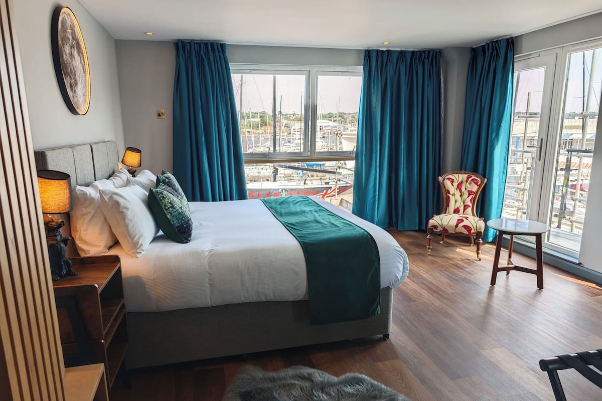 Habitación de hotel con cama, una silla, una mesa y vista a un puerto deportivo.