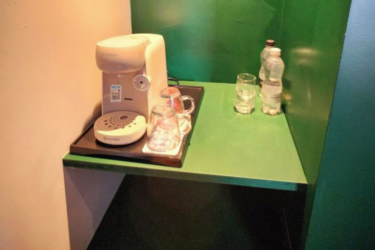 A coffee machine, a glass carafe, and two bottles on a green counter.