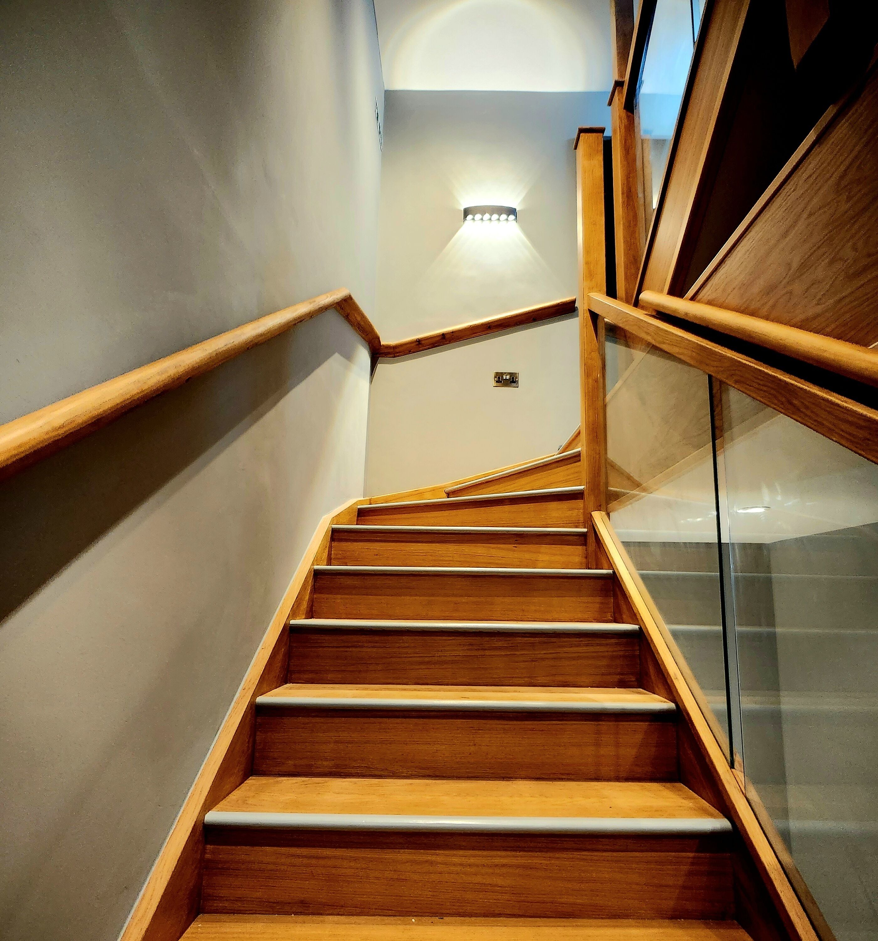 Una escalera de madera con barandillas de vidrio y una lámpara en la parte superior.