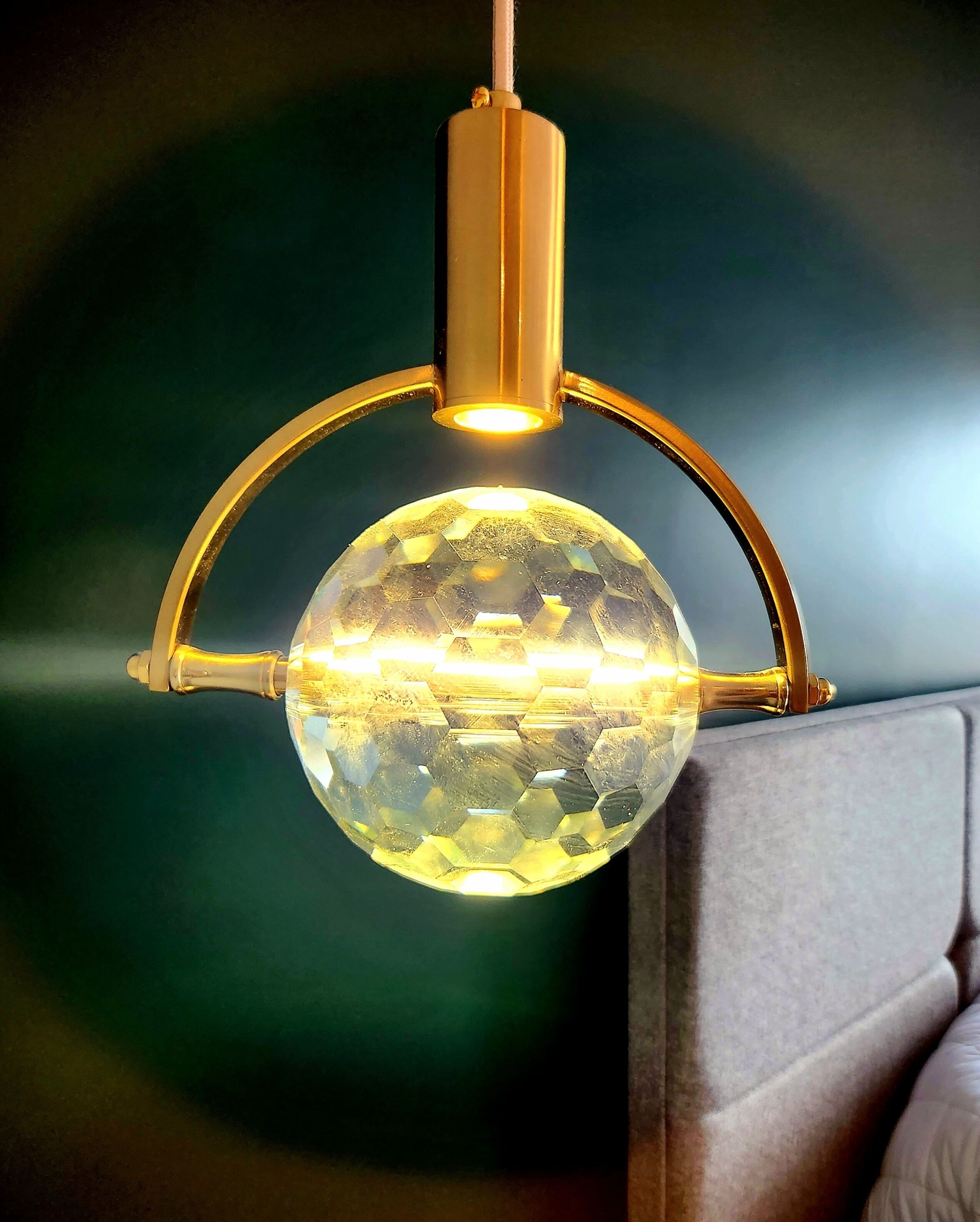A pendant light fixture with a spherical glass element and a gold-colored metal frame.