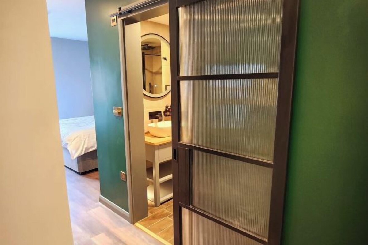 A hotel room with a bed, a bathroom with a mirror, and a sliding door with a textured panel.