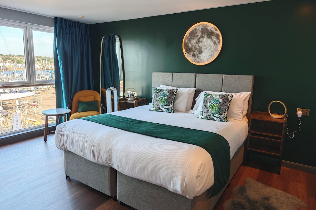 Un hotel moderno con una cama grande, vistas al puerto deportivo y al paisaje urbano.