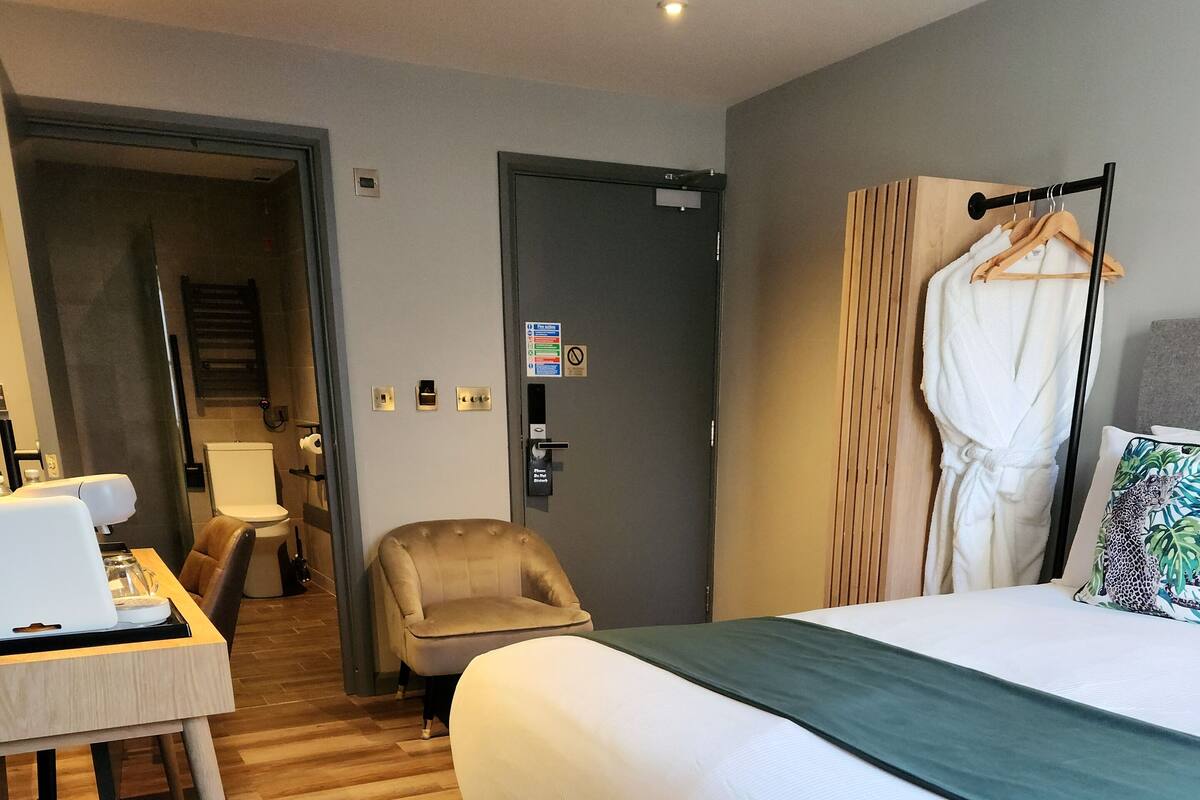 Habitación de hotel con una cama, un escritorio con una computadora portátil, una silla y una bata colgada en un perchero.