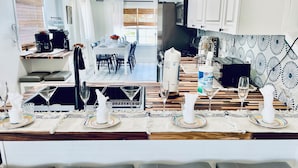 A modern kitchen with white cabinets, a dining area with a table set for four, and a bar area with stools and glasses. - Only 4 bedroom with a view of Main Street located in the Downtown Core District (Dunedin)