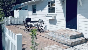 A white house with a dark front door, a patio with a table and chairs, and a white picket fence. - Only 4 bedroom with a view of Main Street located in the Downtown Core District (Dunedin)