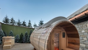 Eine Sauna mit gewölbtem Holzbau, Holzbänken im Inneren und einer Steinsäule rechts.