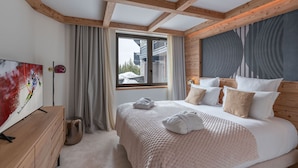 Ein Schlafzimmer mit Holzboden, einem großen Fenster, einem Bett mit Kissen, einem Nachttisch und einem Bild an der Wand.