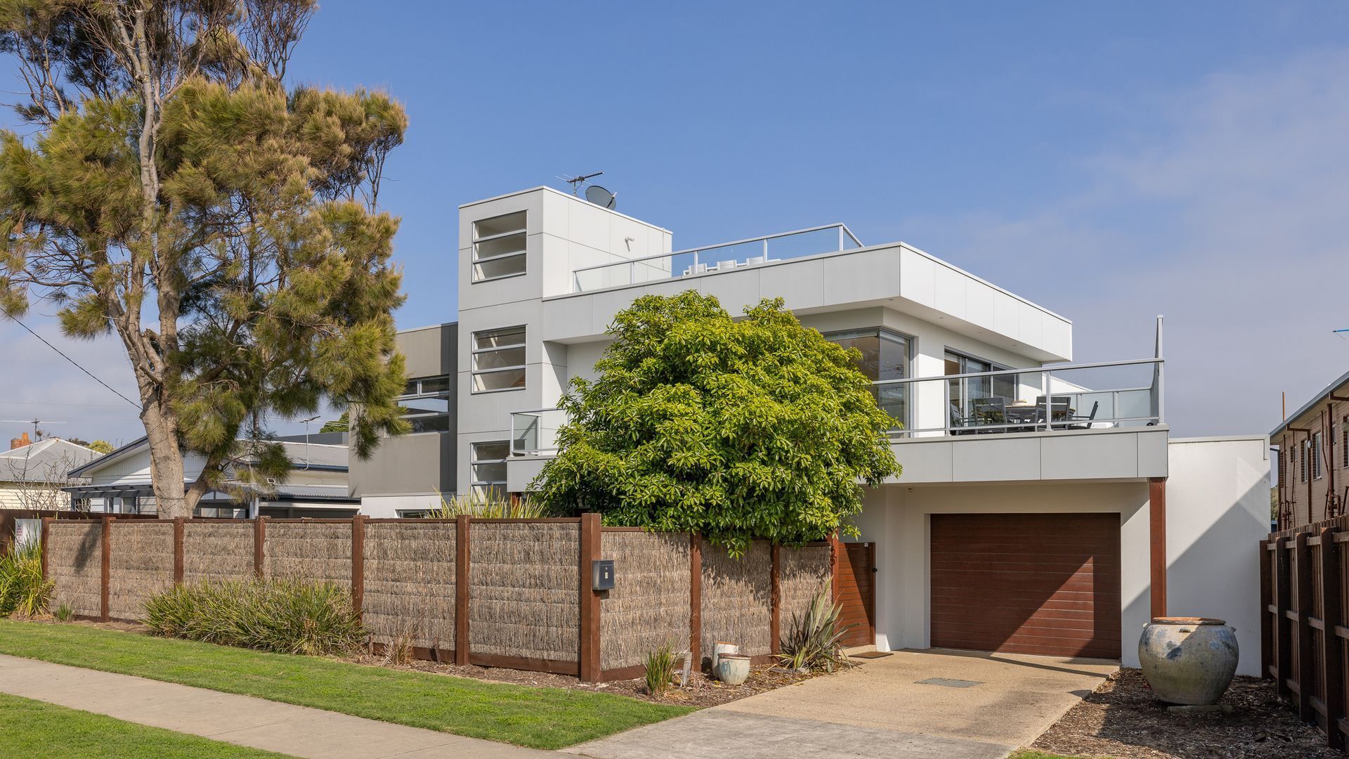 Une maison moderne à deux étages, dotée d’un toit plat, d’un grand arbre à l’avant et d’un garage.
