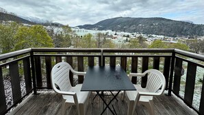 A wooden deck with a table and two chairs, overlooking a snowy landscape with a river and buildings. - Lovely 2-room apartment, south balcony, mountain view, WIFI, 4 pax (Villard-de-Lans)