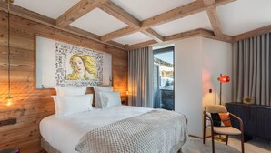 Un dormitorio con techo de madera, una cama grande con ropa blanca, una obra de arte colgada en la pared, un escritorio con una silla y vistas a través de una ventana.