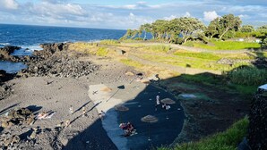 A beach with rocky terrain, a few people, and a view of the ocean. - ENTRE MUROS (Ribeira Grande)