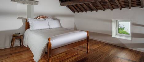 A bedroom with a wooden bed, a nightstand, and a window with a view of greenery.