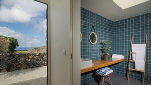 A bathroom with a wooden vanity, a towel rack, and a view of the sea through a glass door. - ENTRE MUROS (Ribeira Grande)