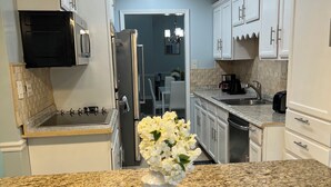 Una cocina moderna con encimeras de granito, armarios blancos, un refrigerador de acero inoxidable y un microondas.