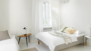 Un dormitorio con cama, mesitas de noche, una ventana con cortinas y una lámpara colgante.