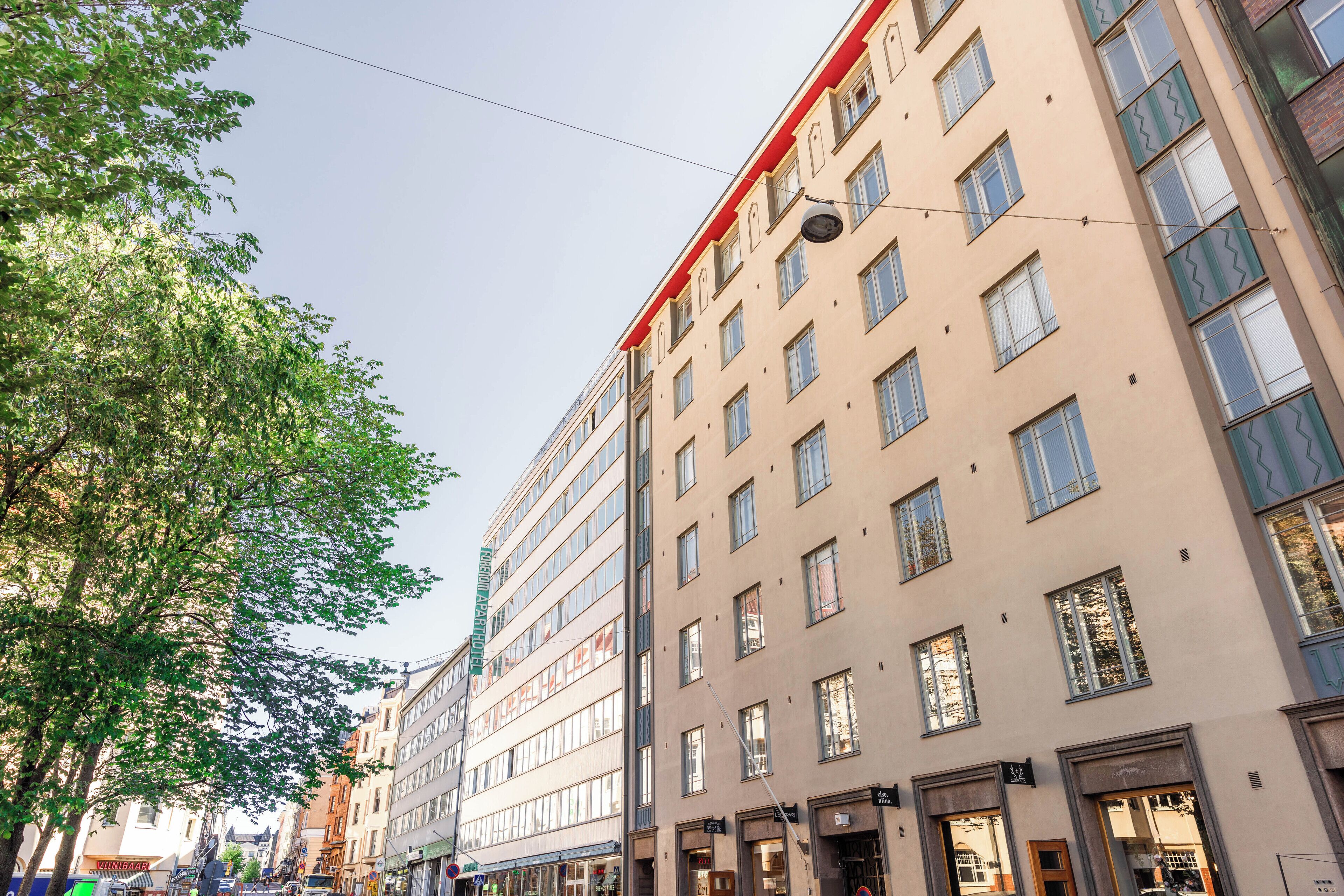 A multi-story building with a beige facade, multiple windows, and a red trim at the top.