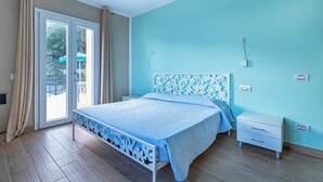 Een slaapkamer met een bed, nachtkastje, dressoir en een schuifdeur naar een buitenruimte.