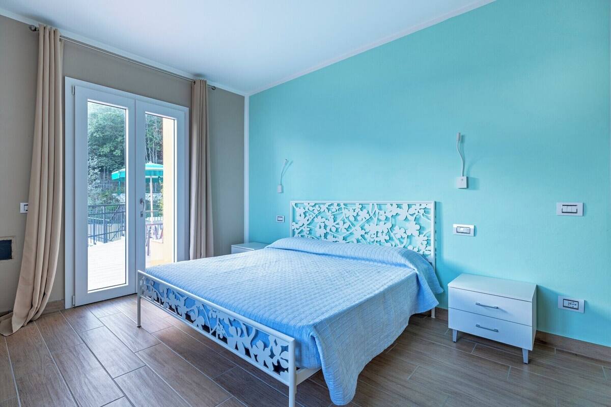 Ein Schlafzimmer mit einem Bett, einem Nachttisch, einer Kommode und einer Glastür, die zu einem Außenbereich führt.