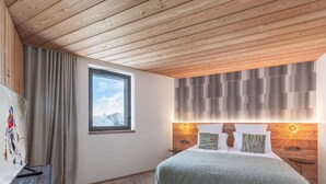 A bedroom with a wooden ceiling, a large bed with a green blanket, a window with a view of mountains, and a wall with a geometric pattern. - New ski-in/ski-out duplex in Courchevel with parking (Courchevel 1850)