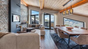 A modern living room with a stone wall, wooden ceiling, and large windows offering a mountain view. - New ski-in, ski-out duplex with SPA in Courchevel 1850 (Courchevel 1850)