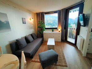 A cozy living room with a sofa, a small table, a TV, and a window with a view of the outdoors.