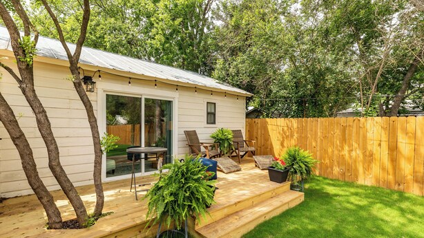 Un patio trasero con terraza de madera, zona de comedor con sillas y cercado de madera.
