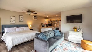 Un dormitorio con cama, sofá gris, cómoda blanca y televisor en la pared.