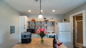 Una cocina con armarios de madera, encimera de madera, cafetera, refrigerador y un florero con flores.
