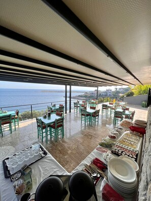 A terrace with tables and chairs, a buffet setup, and a view of the sea.