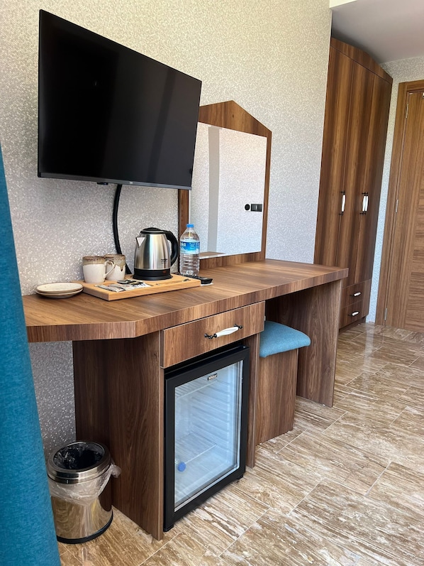 A compact kitchenette with a flat-screen TV, a coffee maker, a water bottle, and a mini-fridge.