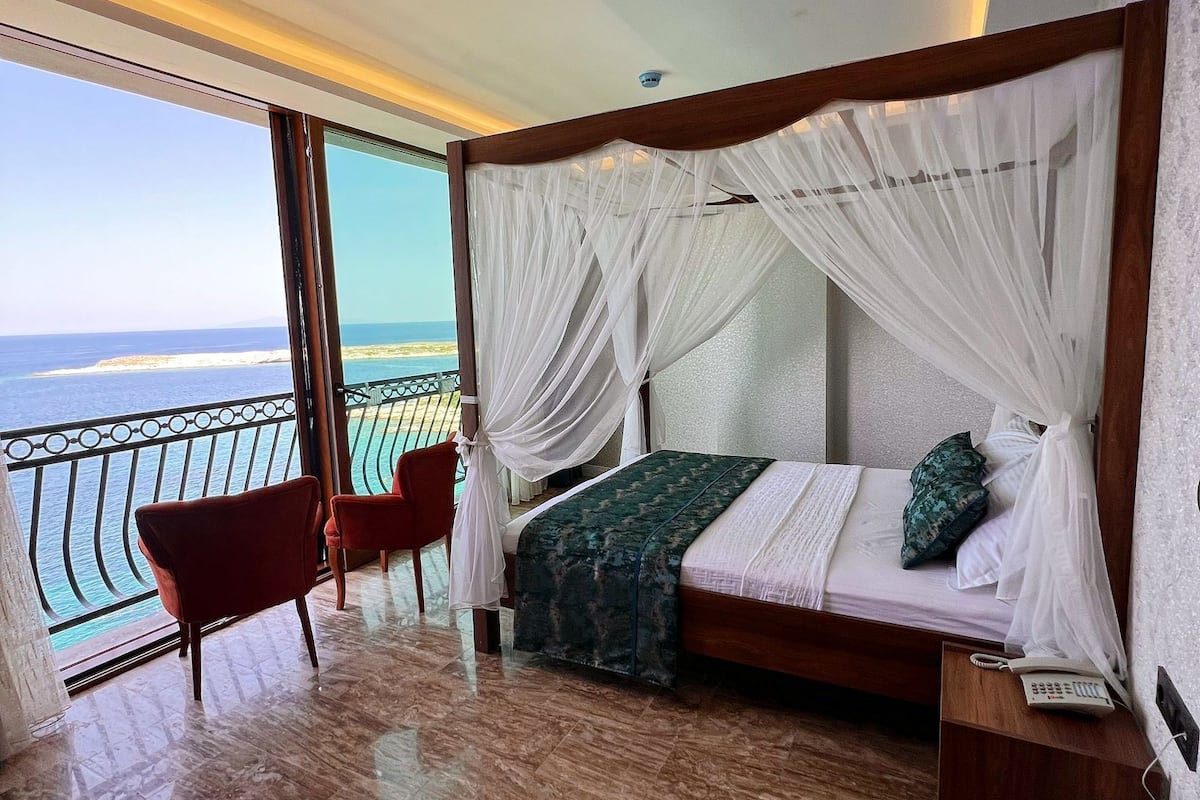 A bedroom with a bed, a chair, a bedside table, and a view of the sea.