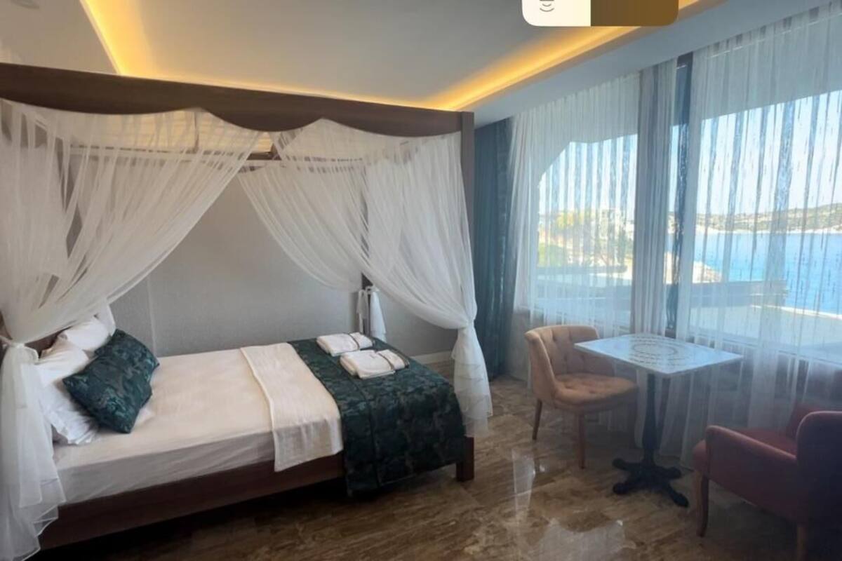 A bedroom with a bed, a table, and a chair, and a view of the sea.