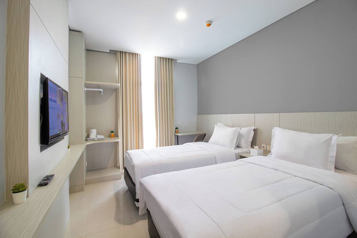 A hotel room with two beds, a TV, a small table with a coffee maker, and a bedside table with a lamp.