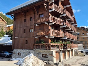 A multi-story wooden building with balconies, stone foundation, and a ski slope in the background.