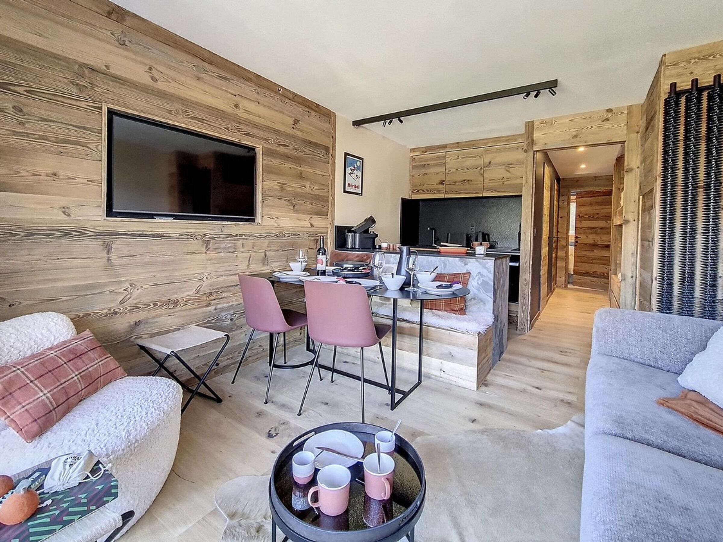 A cozy living room with a fireplace, a dining area with pink chairs, and a kitchen with wooden cabinets.